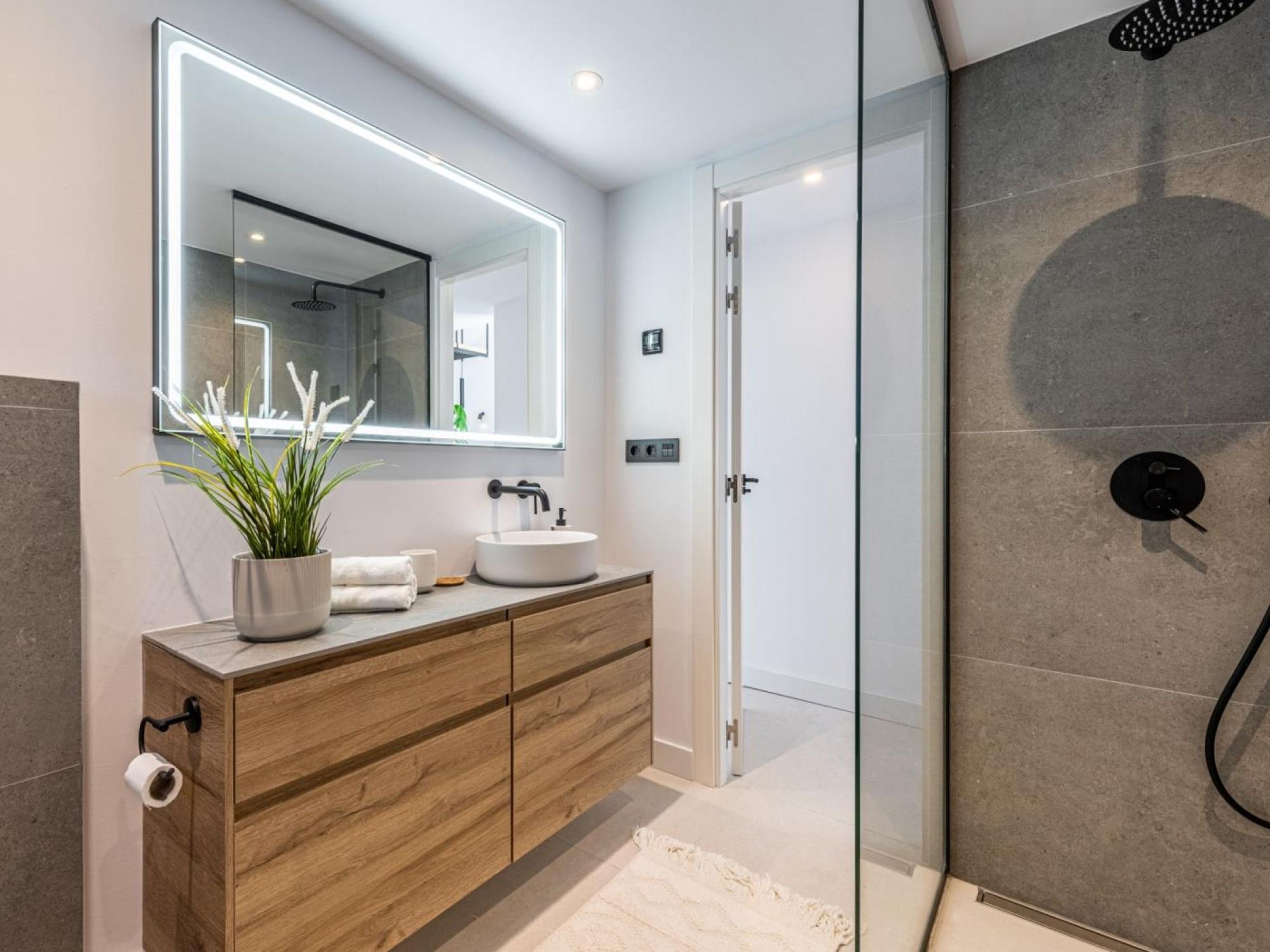 A modern bathroom with a wooden vanity, a large mirror, and a glass shower enclosure.