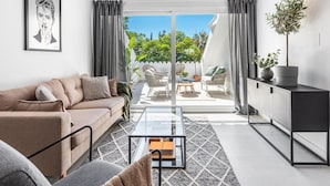 A modern living room with a sofa, coffee table, and a view of an outdoor patio with seating and plants. - Agrupadas Beautiful Duplex With Amazing Location (Marbella)