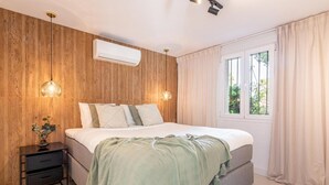 A bedroom with a wooden wall, a bed with a green blanket, bedside tables, and a window with curtains. - Agrupadas Beautiful Duplex With Amazing Location (Marbella)