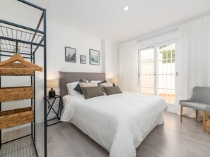 A bedroom with a bed, a chair, a hanging rack, and a window with curtains. - Se or o de Aloha 2 Bedroom (Marbella)