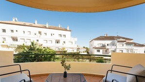 A balcony with a sofa and a small table, overlooking a residential area with white buildings and a clear sky. - Se or o de Aloha 2 Bedroom (Marbella)