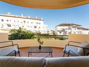 A balcony with a sofa and a small table, overlooking a residential area with white buildings and a clear sky. - Se or o de Aloha 2 Bedroom (Marbella)