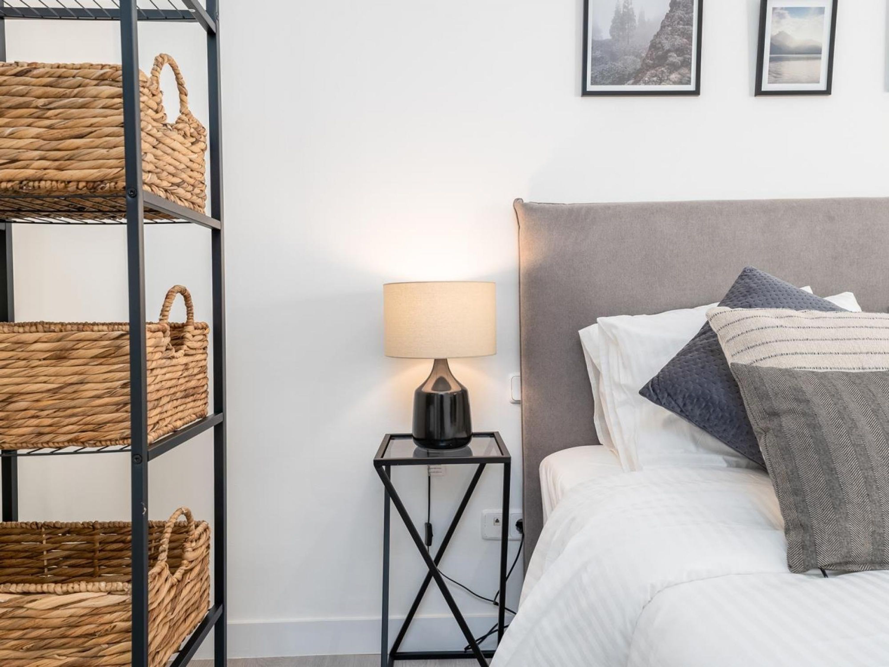 A neatly arranged bedroom with a bed, a bedside table with a lamp, and a wall-mounted shelf with baskets.