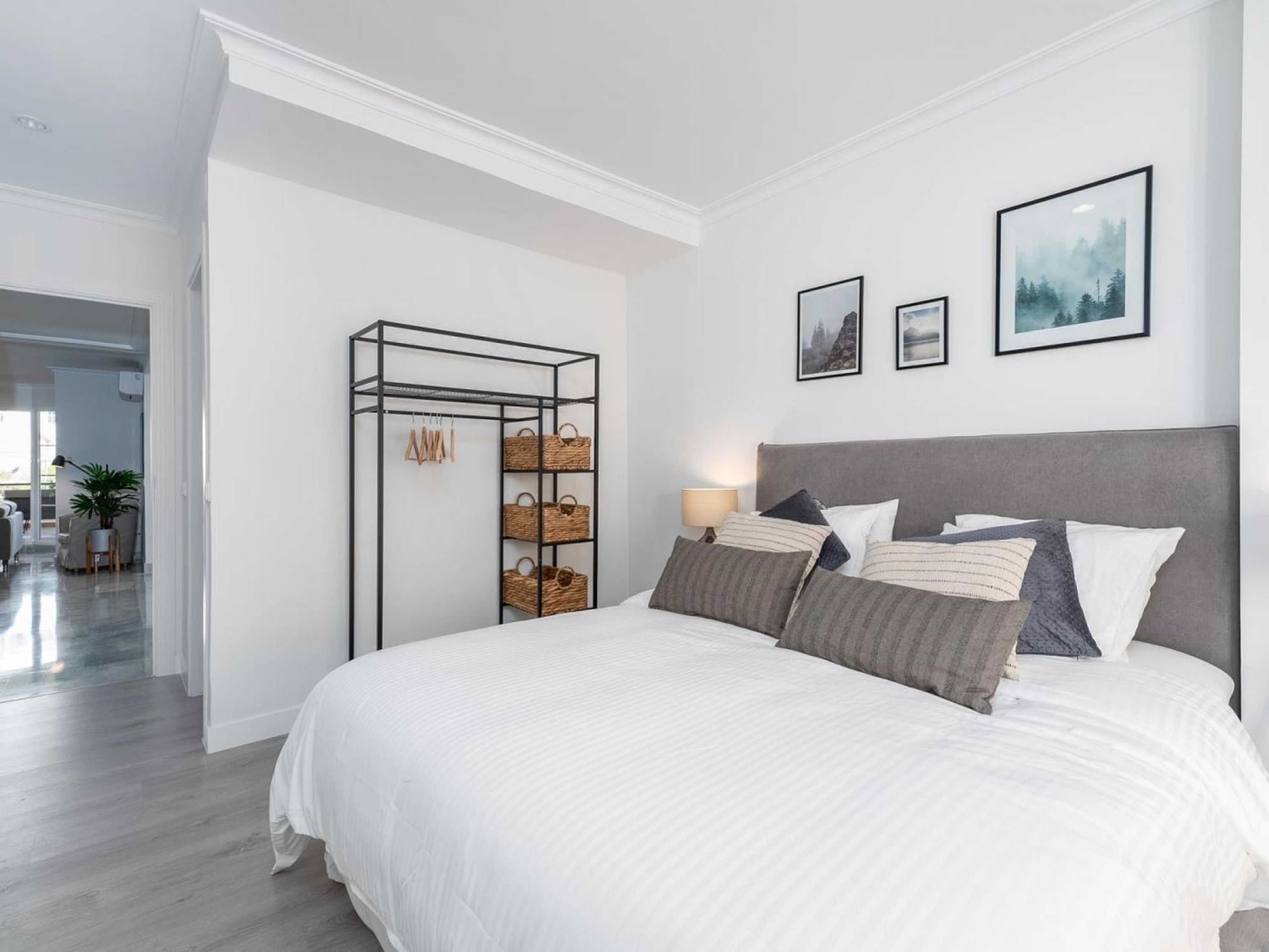 A modern bedroom with a large bed, a metal storage unit with baskets, and two framed pictures on the wall.