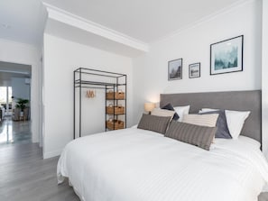 Ein modernes Schlafzimmer mit einem großen Bett, einer Metall-Aufbewahrungseinheit mit Körben und zwei gerahmten Bildern an der Wand.