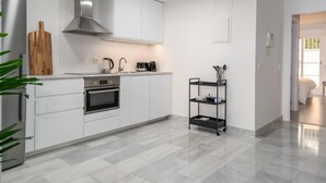 A modern kitchen with white cabinets, a stainless steel range hood, a coffee maker, and a black metal shelf. - Se or o de Aloha 2 Bedroom (Marbella)