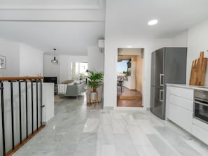 A modern kitchen with a refrigerator, a wooden cutting board, and a dining area with a table and chairs. - Se or o de Aloha 2 Bedroom (Marbella)