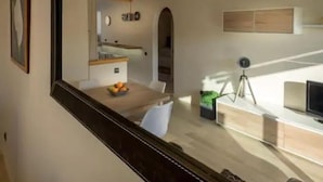 A modern interior with a large mirror reflecting a dining area, a small kitchen, and a desk with a computer and a tripod. - Beachfront Sunny Apartment Sea Mountain View (Castelldefels)