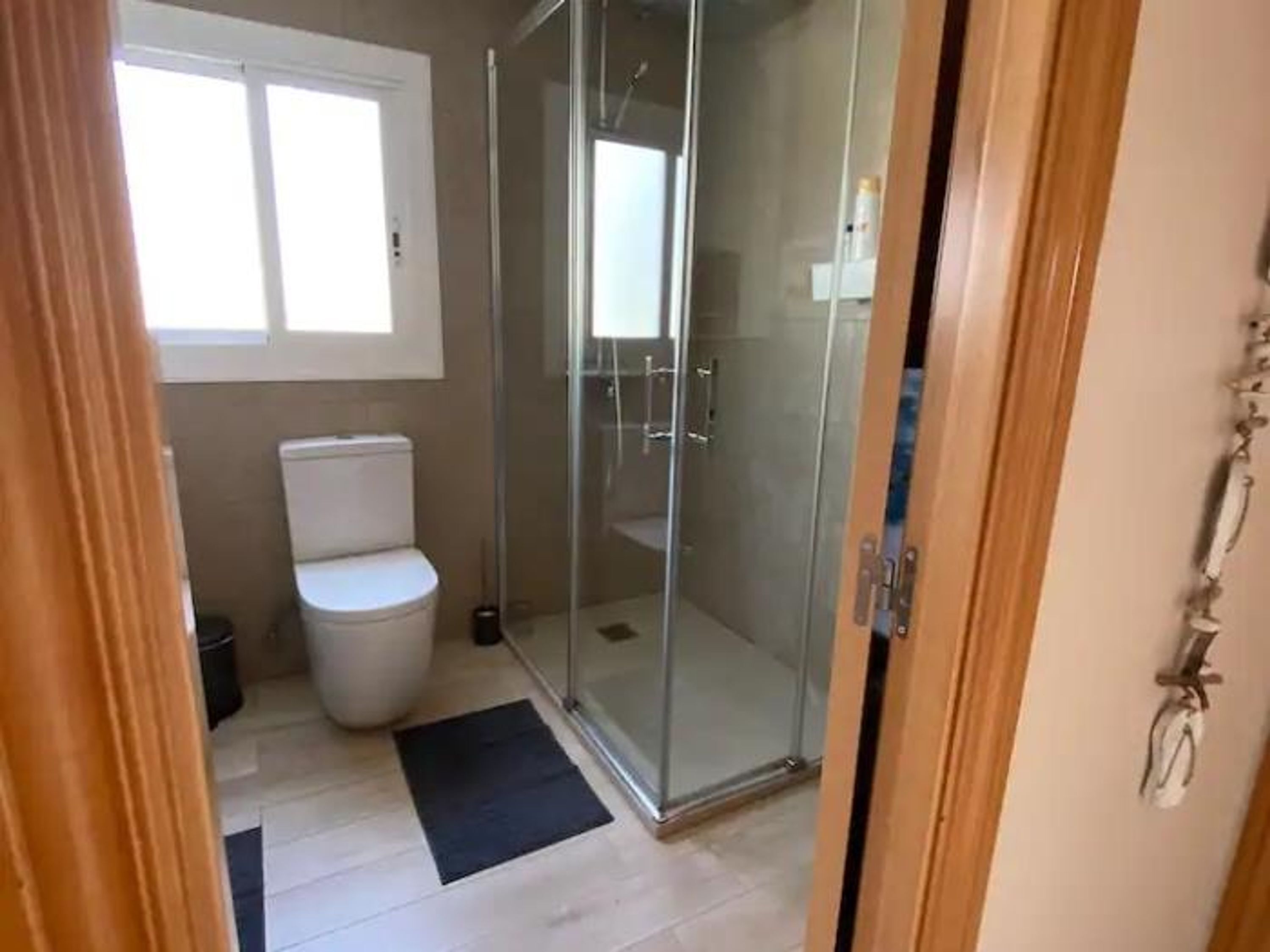 Een badkamer met toilet, een douchecabine van glas en een zwarte mat op de vloer.