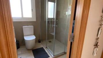 Een badkamer met toilet, een douchecabine van glas en een zwarte mat op de vloer.