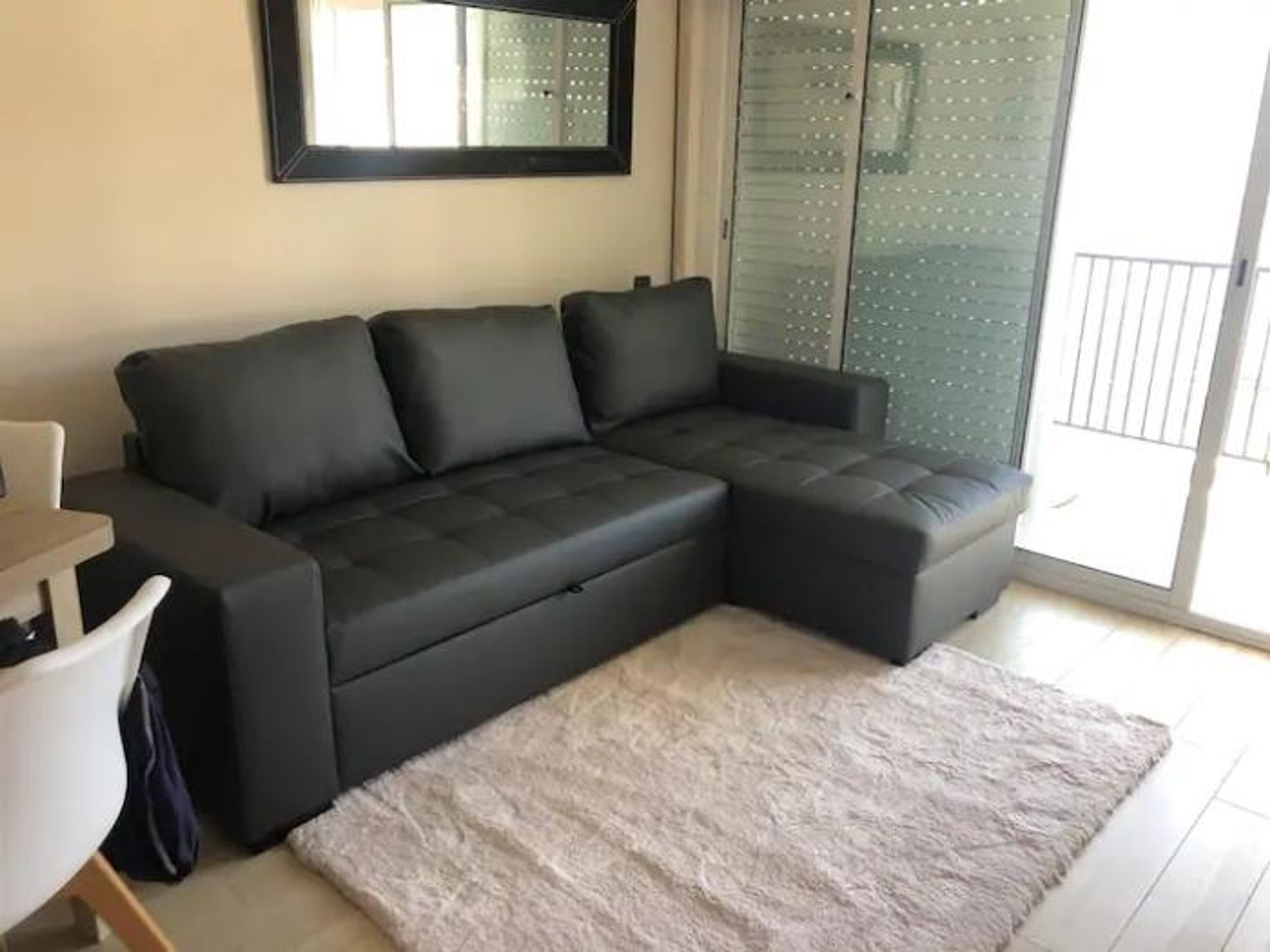 Un salón moderno con un sofá seccional gris oscuro, una mesita blanca y una alfombra gris suave.