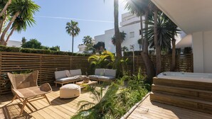 An outdoor patio with wooden flooring, a seating area with cushions, and a hot tub.