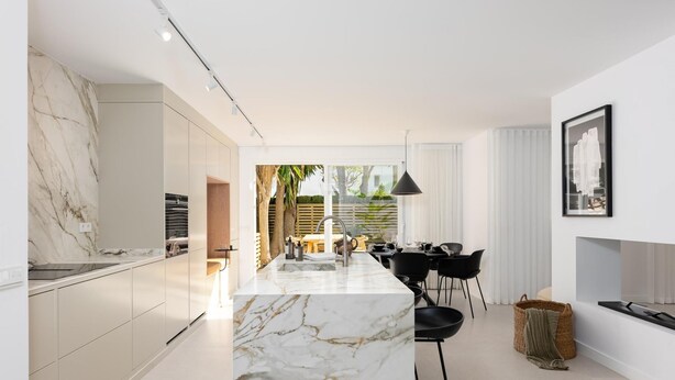 A modern kitchen with marble countertops, a dining area with black chairs, and a view of the outdoors.