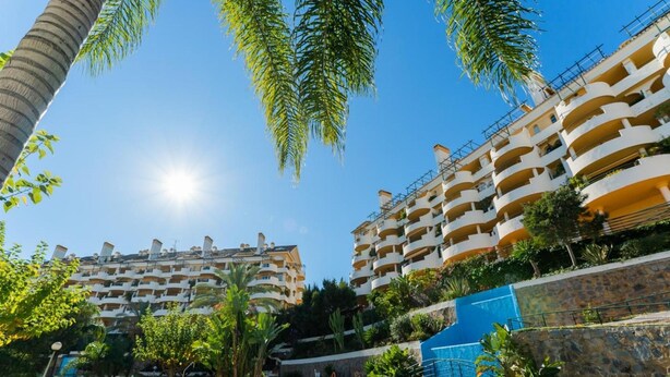 Un hotel con diversi balconi, una piscina e vegetazione lussureggiante.