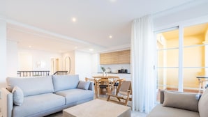 Un soggiorno moderno con un divano azzurro, un tavolino da caffè beige e un altro divano beige. C'è una zona pranzo con un tavolo e sedie in legno. La stanza presenta una scala che conduce a un piano superiore.