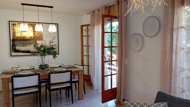 Zona pranzo con tavolo in legno apparecchiato per quattro persone, due lampade a sospensione e un grande quadro astratto.