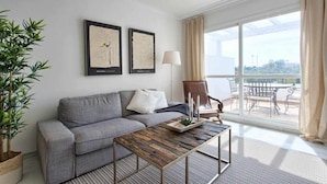 Una sala de estar moderna con un sofá gris, una mesa de centro de madera y un ventanal con vistas a un balcón.