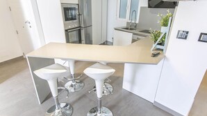 A modern kitchen with a central island, bar stools, a built-in oven, and a Samsung TV.