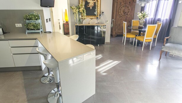 A modern kitchen with a central island, dining area with yellow chairs, and a large framed religious painting.