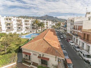 Une rue résidentielle bordée d’une rangée de bâtiments blancs, avec une piscine bleue et une chaîne de montagnes en arrière-plan.