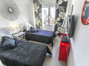 Une chambre avec deux lits, une armoire rouge, une télévision et un miroir décoratif.