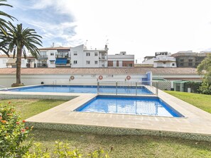 Une piscine dotée d’une terrasse carrelée, entourée d’une pelouse et d’un palmier.