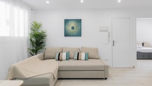 Een moderne woonkamer met een beige modulaire bank, een grote potplant en een abstract schilderij aan de muur.