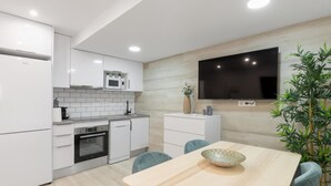 Een moderne keuken met witte kasten, een ingebouwde magnetron, een vaatwasser en een grote flatscreen televisie aan de muur.
