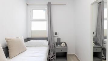 Un dormitorio pequeño y moderno con cama, mesita de noche, espejo y ventana con cortinas.