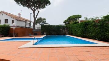 A rectangular swimming pool with a tiled deck, surrounded by a hedge and a tree.