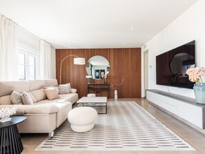 Un salon moderne avec un canapé, un pouf et un téléviseur fixé au mur.