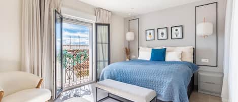 Un dormitorio moderno con una cama grande, un banco, una silla y un balcón con vistas.