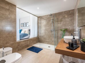 A modern bathroom with a glass shower enclosure, a wooden vanity, a white sink, and a toilet.