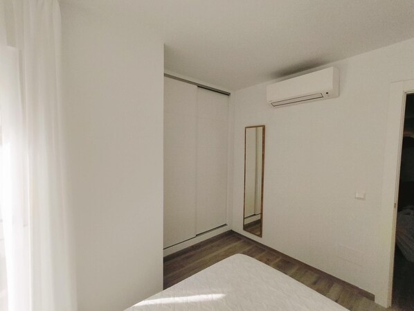 A bedroom with a bed, a wardrobe, a mirror, and an air conditioning unit.