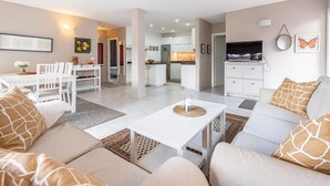 A modern living room with a sofa set, a dining area with a table and chairs, a kitchen in the background, and a TV on a cabinet. - Sol y Paz 3 Family Apartment With Great Location (Marbella)