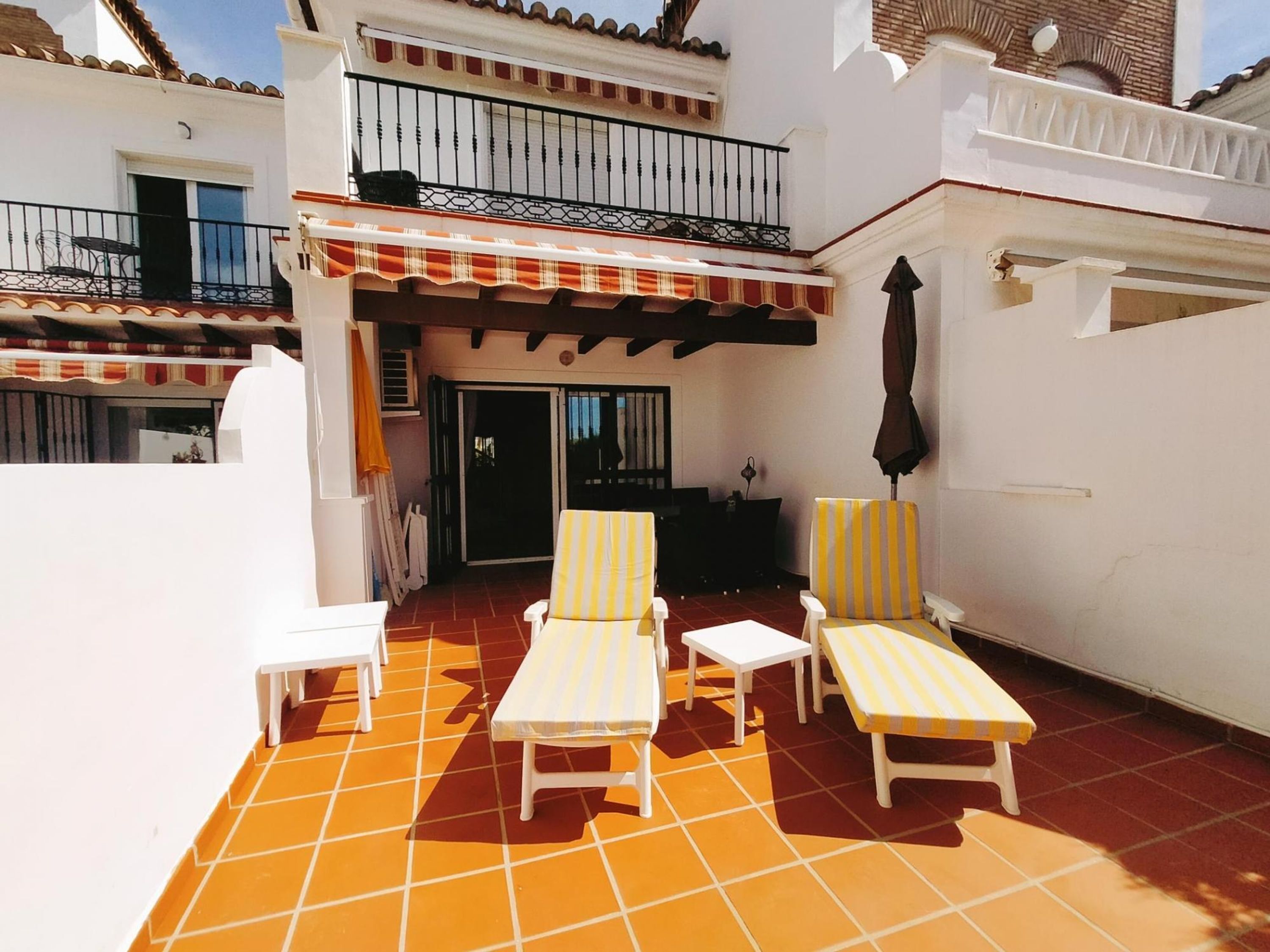 A patio with two sun loungers and a table, a covered area with a railing, and a door leading to an interior space.
