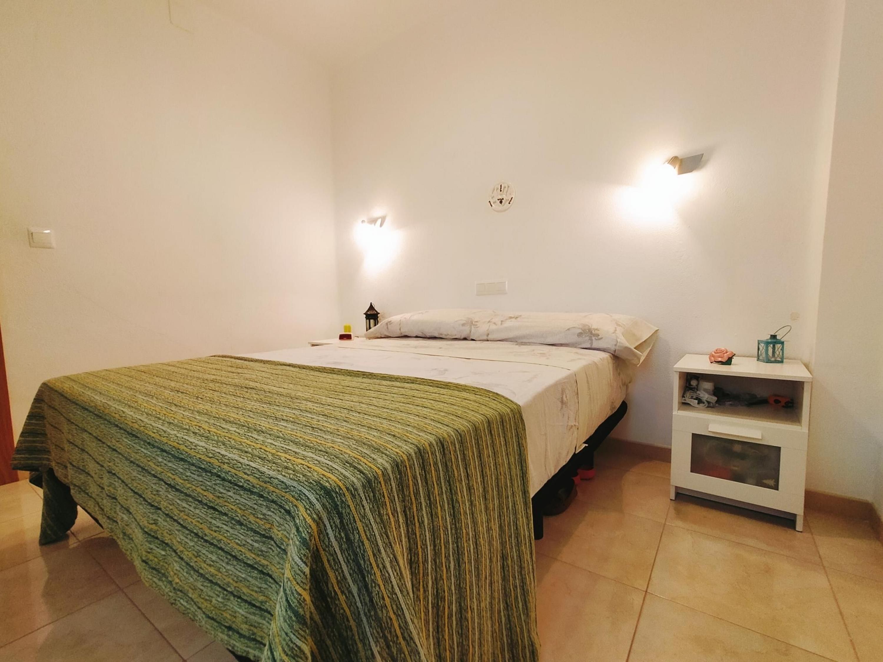 A room with a bed, a nightstand, and a wall-mounted light fixture.