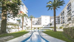 Une piscine à l’eau d’un bleu limpide, entourée de pelouse bien entretenue et de palmiers, avec des immeubles à plusieurs étages en arrière-plan.