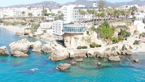 Un hôtel situé sur la côte, avec plusieurs étages, une façade en verre remarquable et un rivage rocheux.
