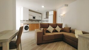 A modern living room with a sofa, a dining table, and a washing machine in the background. - Apartamento Bronce B Centro Nerja Sun (Nerja)