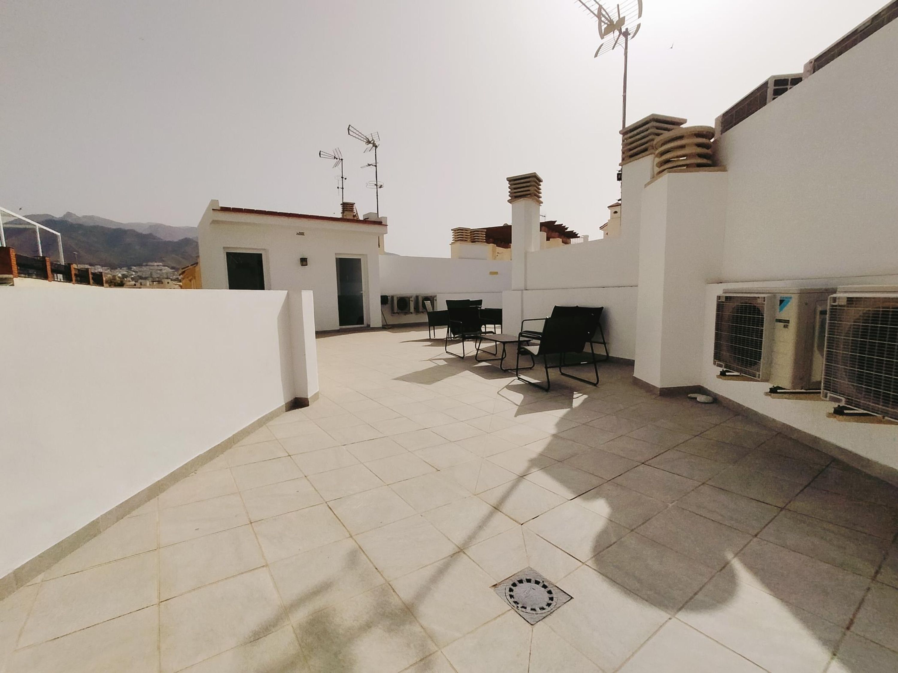 A rooftop terrace with tiled flooring, outdoor seating, and air conditioning units.