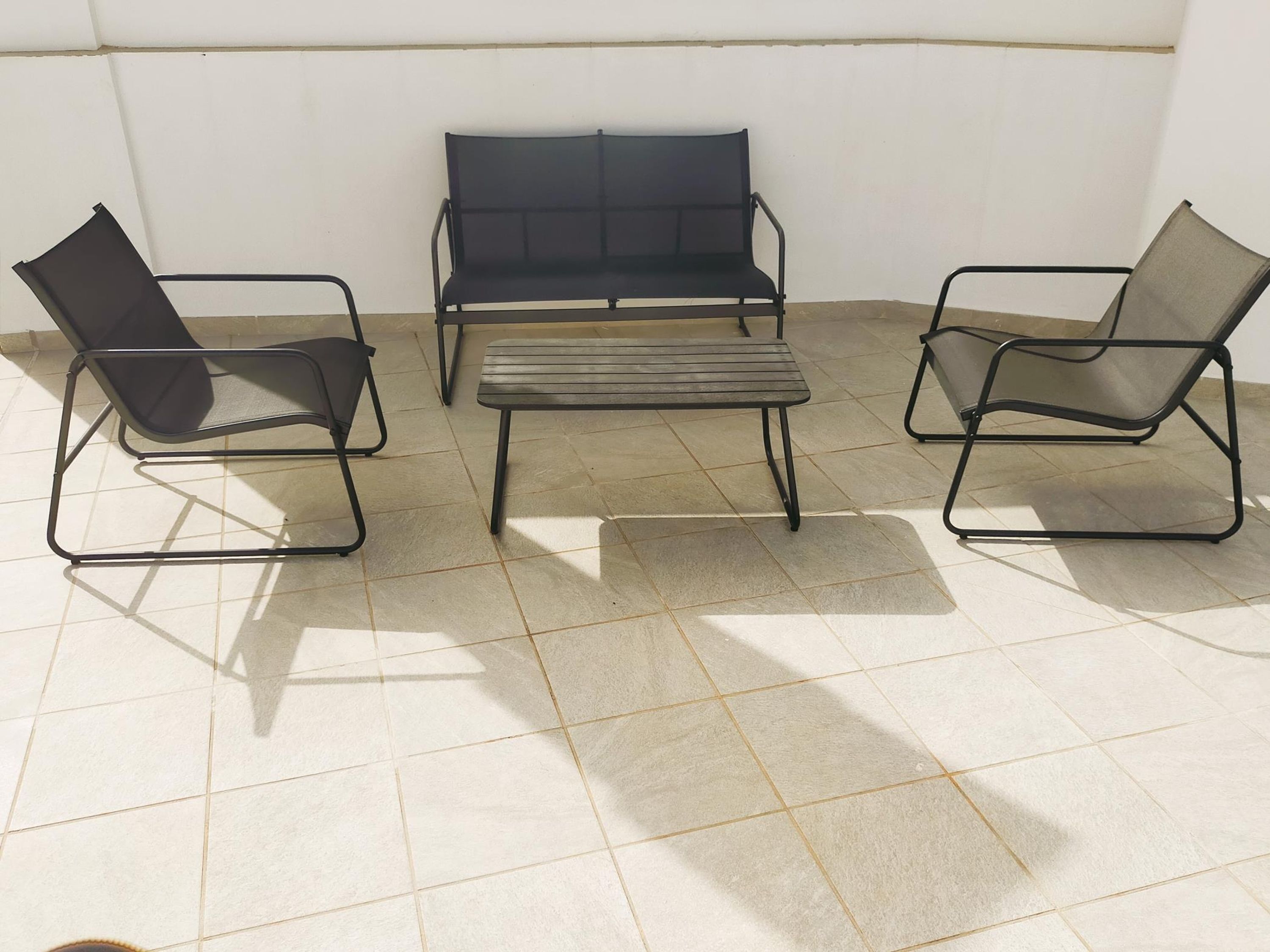 A room with a tiled floor and three metal-framed chairs and a bench.
