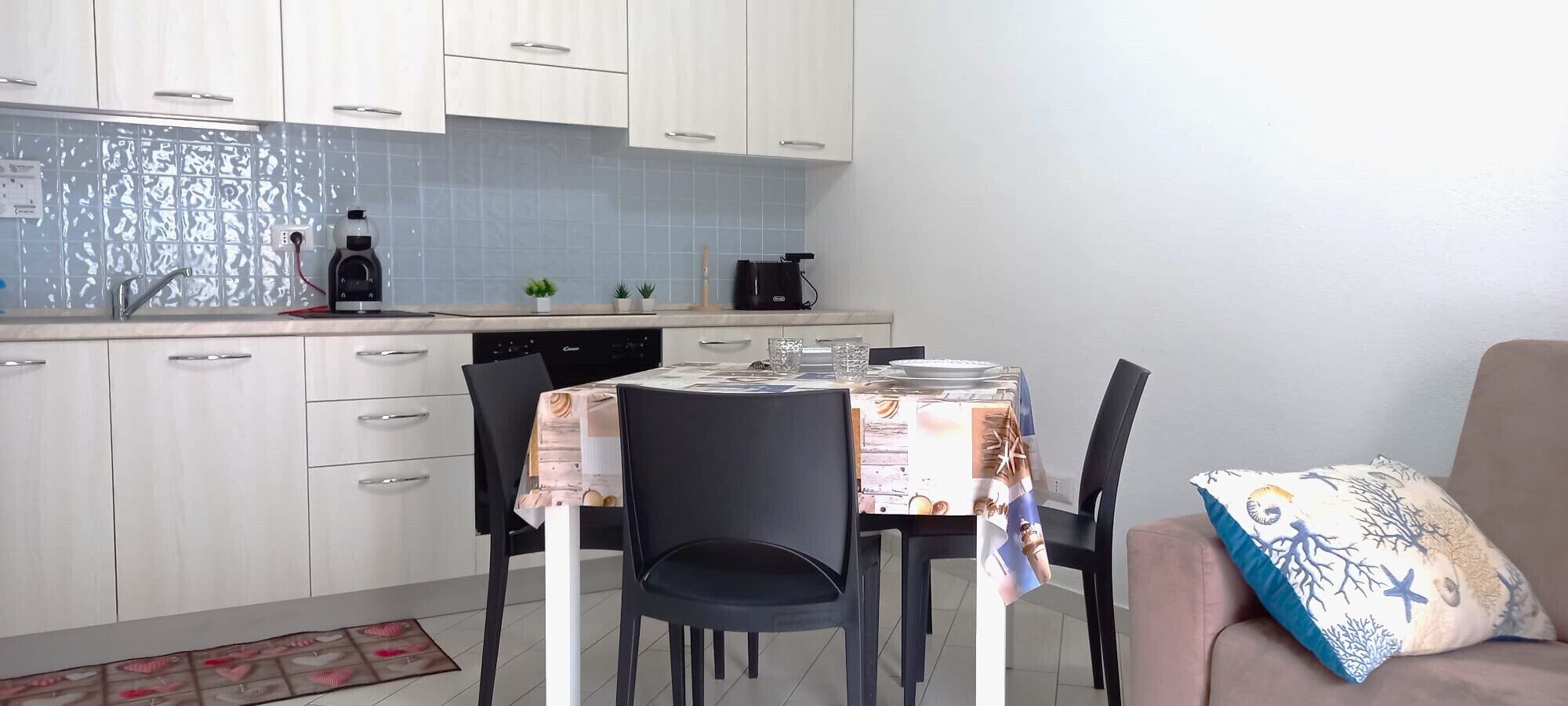 Een moderne keuken met witte kasten, een koffieapparaat en een eettafel gedekt voor vier personen.