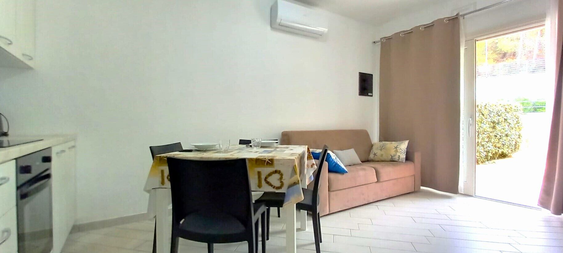 A dining area with a table set for two, a sofa, and a sliding glass door leading to a balcony.