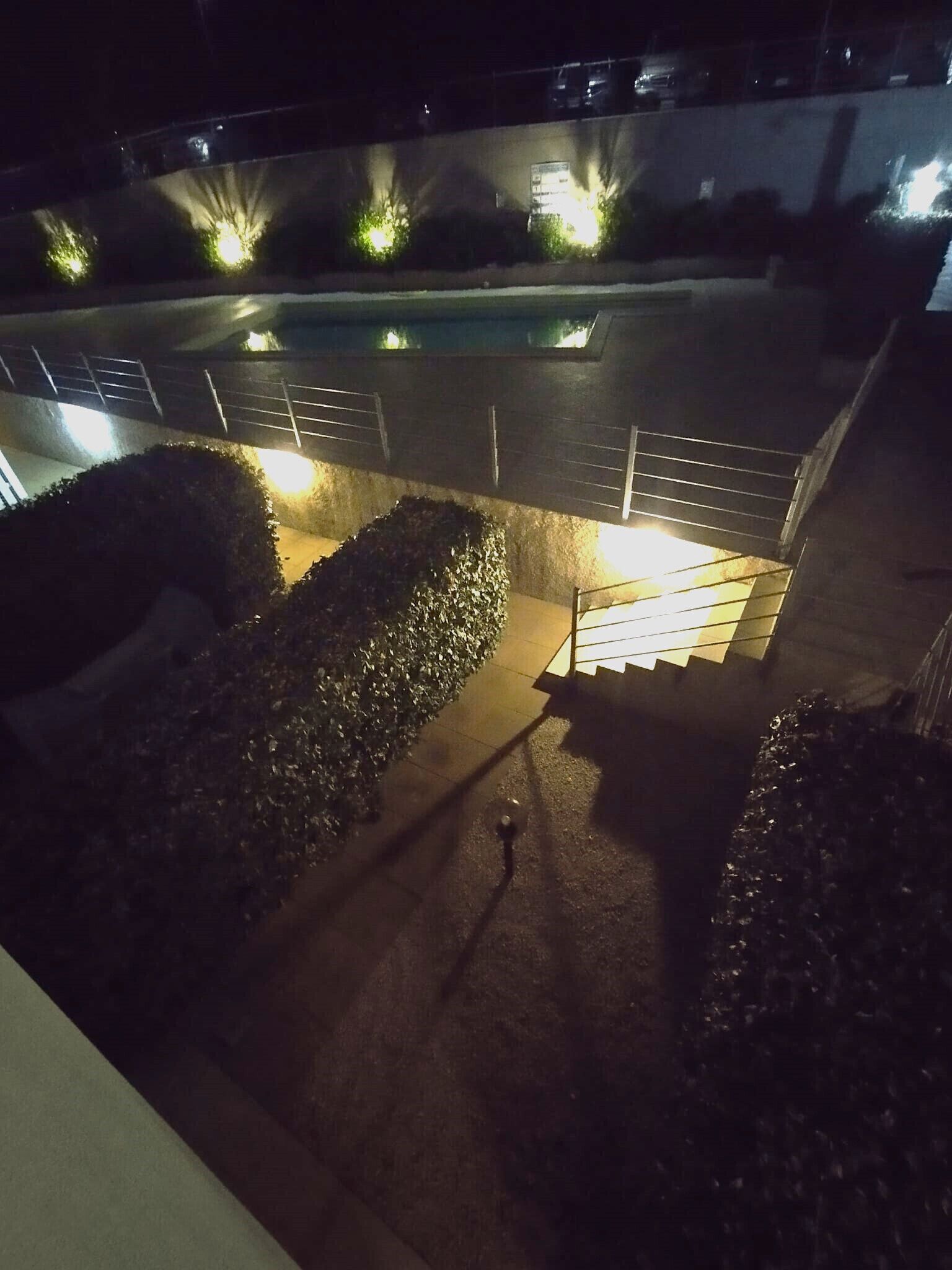 Vista nocturna de un área de piscina con escalones bien iluminados y jardines circundantes.