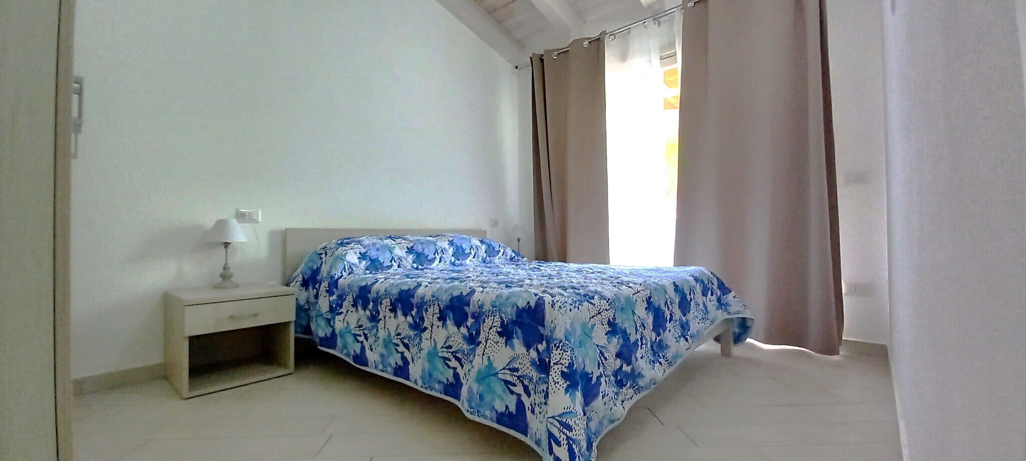 A bedroom with a bed, a nightstand, a lamp, and a window with curtains.