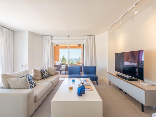 Una sala de estar moderna con sofá, mesa de centro y televisor. Tiene un balcón con vistas.