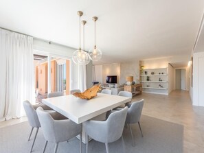 A spacious dining area with a white table, grey chairs, and a wooden centerpiece.