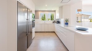 A modern kitchen with white cabinetry, a stainless steel refrigerator, and a window providing a view of greenery and mountains.