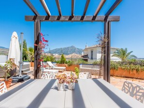 An outdoor patio with a pergola, white table, chairs, and potted plants.